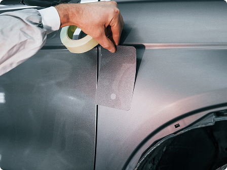 a man comparing a paint color card to a car’s paint finish